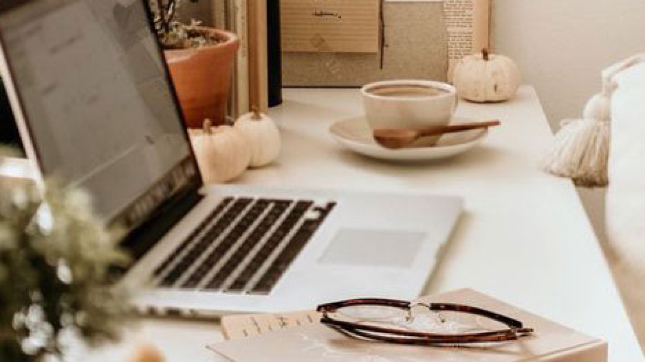 Laptop on a desk next to a coffee and notebook