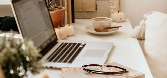 Laptop on a desk next to a coffee and notebook