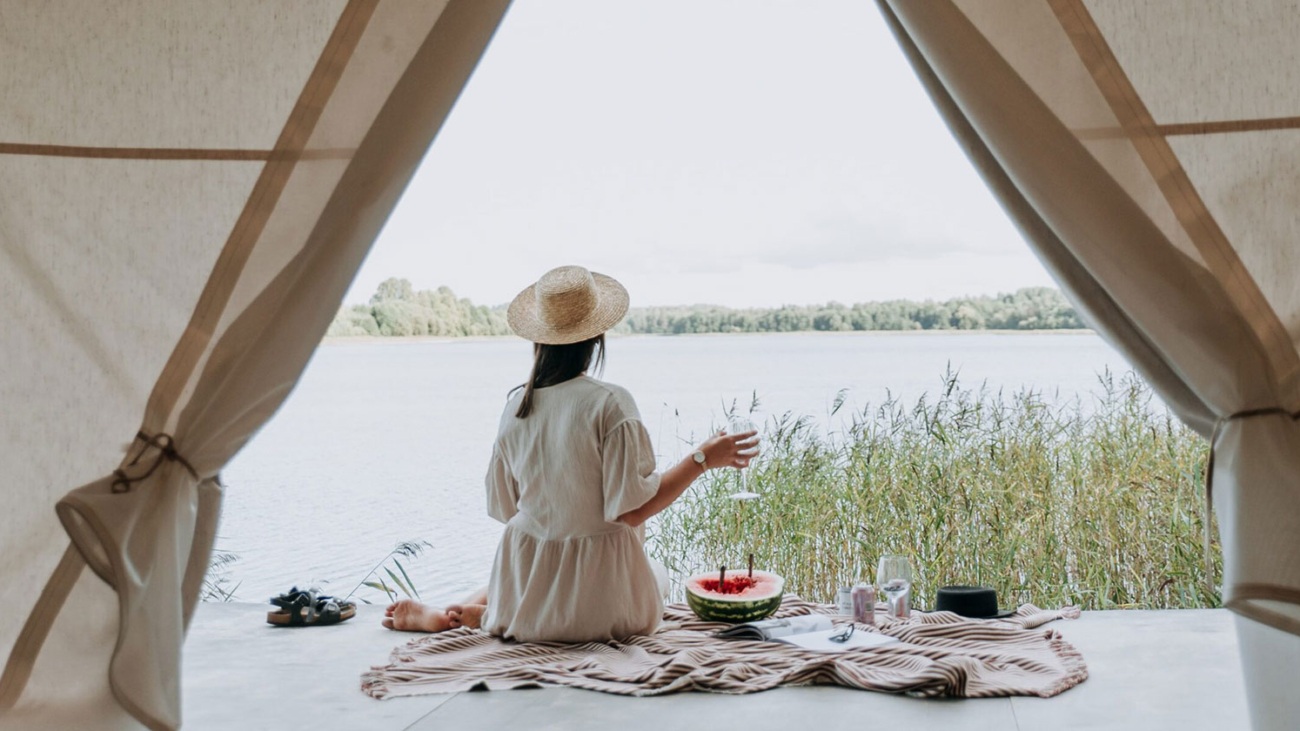 Woman sat having a picnic in the doorway of a glamping tent overlooking the lake