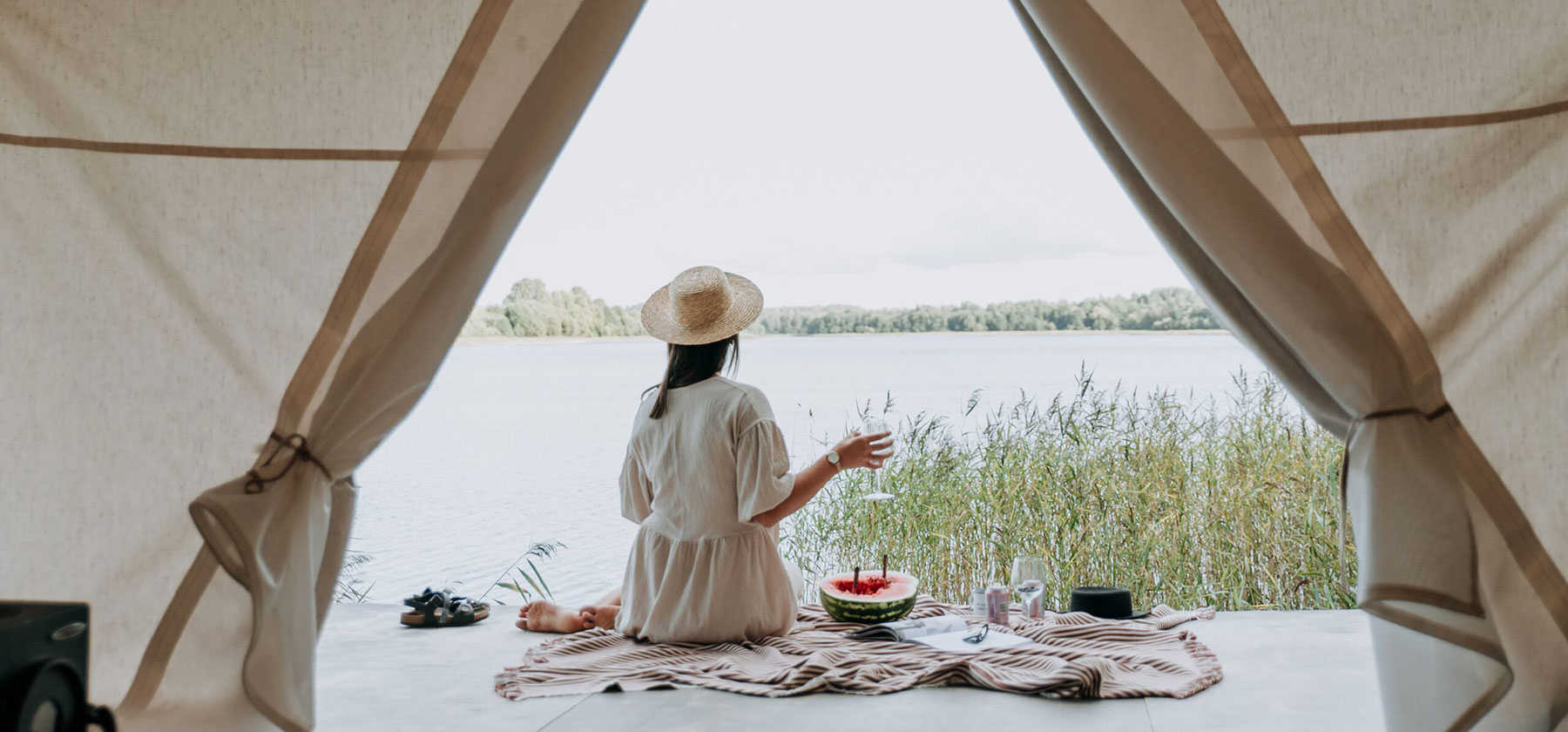Woman sat having a picnic in the doorway of a glamping tent overlooking the lake