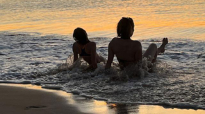 2 people sat in the sea at sunset
