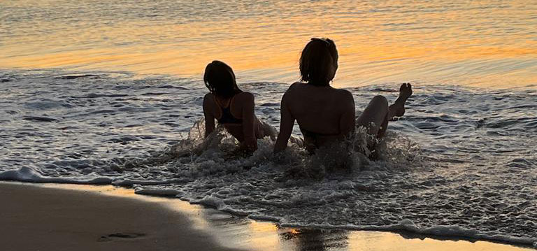 2 people sat in the sea at sunset