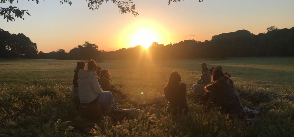 Group sat in a field watching the sunset