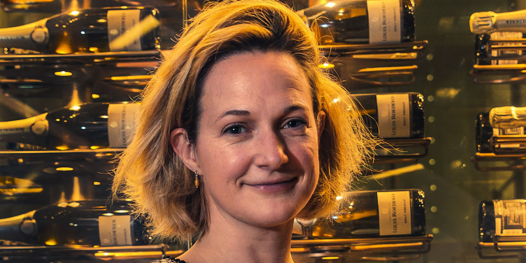 Photo of Lucy stood in front of a display of red wine bottles