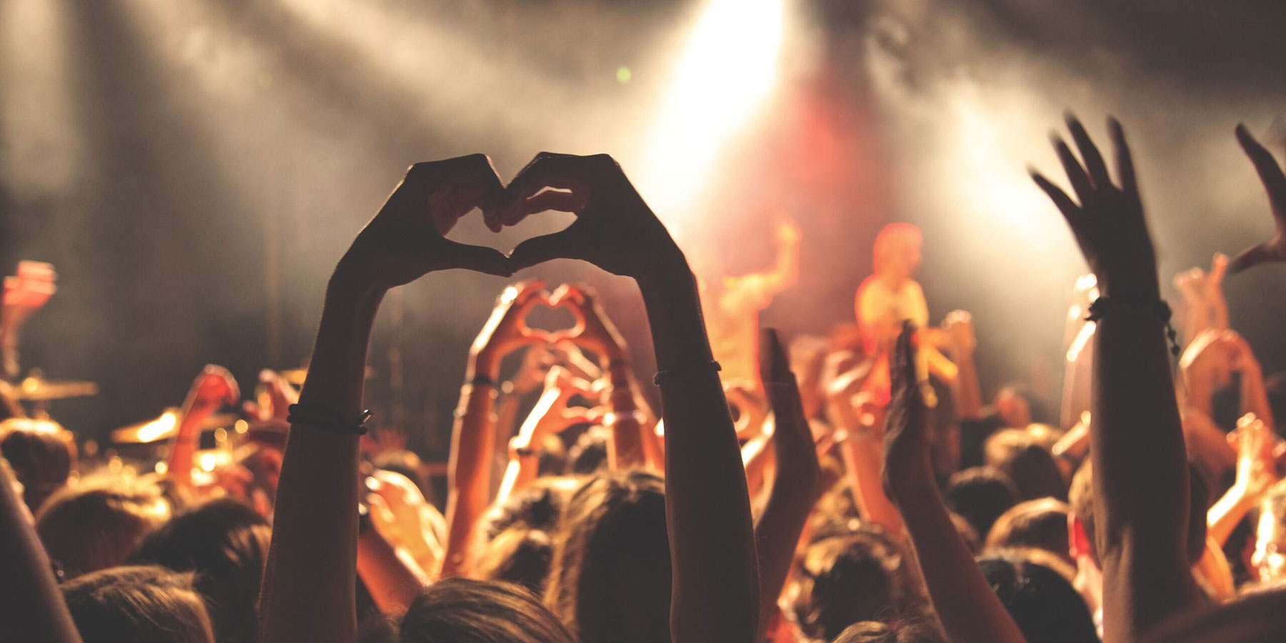 Person making a heart shape with their hands at a concert
