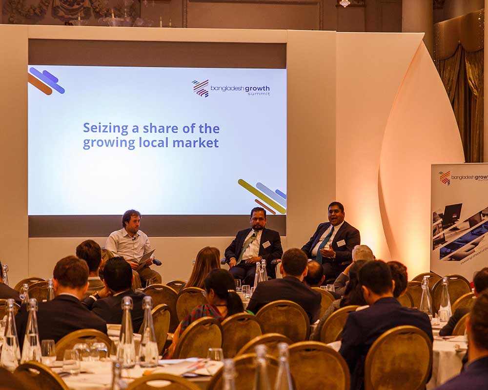 A panel of speakers with a screen sat at the front of a conference